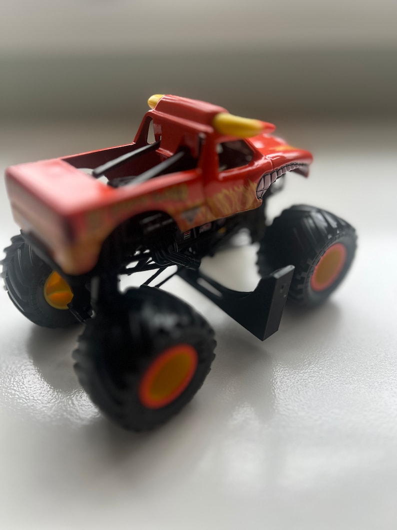 May include: A red and yellow monster truck toy with large black tires and yellow rims. The truck features a bull-like design with horns and flame graphics. The toy is designed for off-road play.