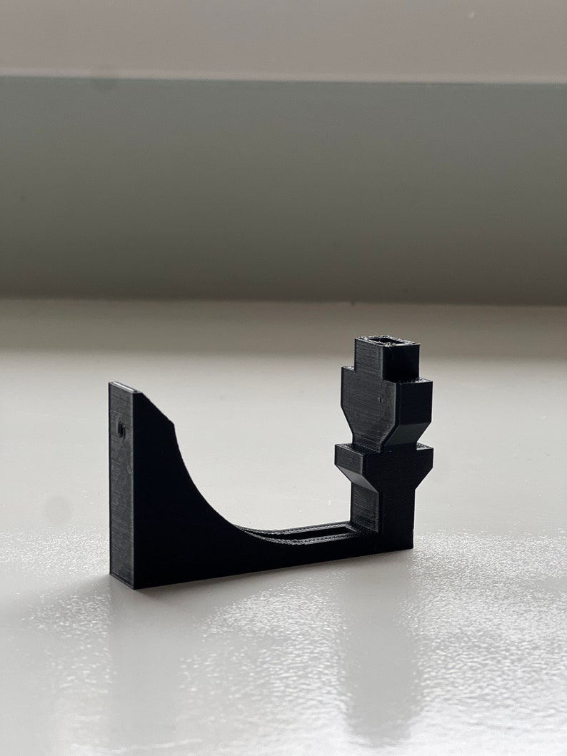 May include: A black 3D-printed bracket with a curved arm and a vertical post. The bracket has a rectangular base with a hole for mounting. The design is simple and functional, likely for holding or supporting an object.