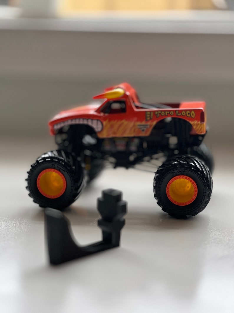 May include: A red and yellow toy monster truck with the words "El Toro Loco" printed on the side. The truck has large black tires with yellow rims and a bull horn on top. A black plastic piece is in front of the truck.