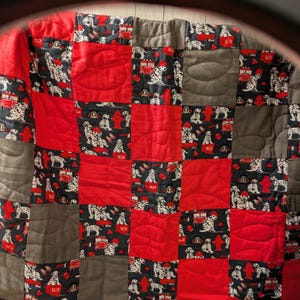 Peut inclure: Une courtepointe rouge et grise en patchwork avec un motif de chien dalmate et de camion de pompiers. La courtepointe est faite de carrés et est matelassée avec un point simple.