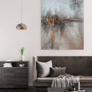 May include: A modern living room interior with a gray sofa, a coffee table, and a gray and gold abstract painting on the wall. The painting has a textured surface and features a horizontal line of gold paint.