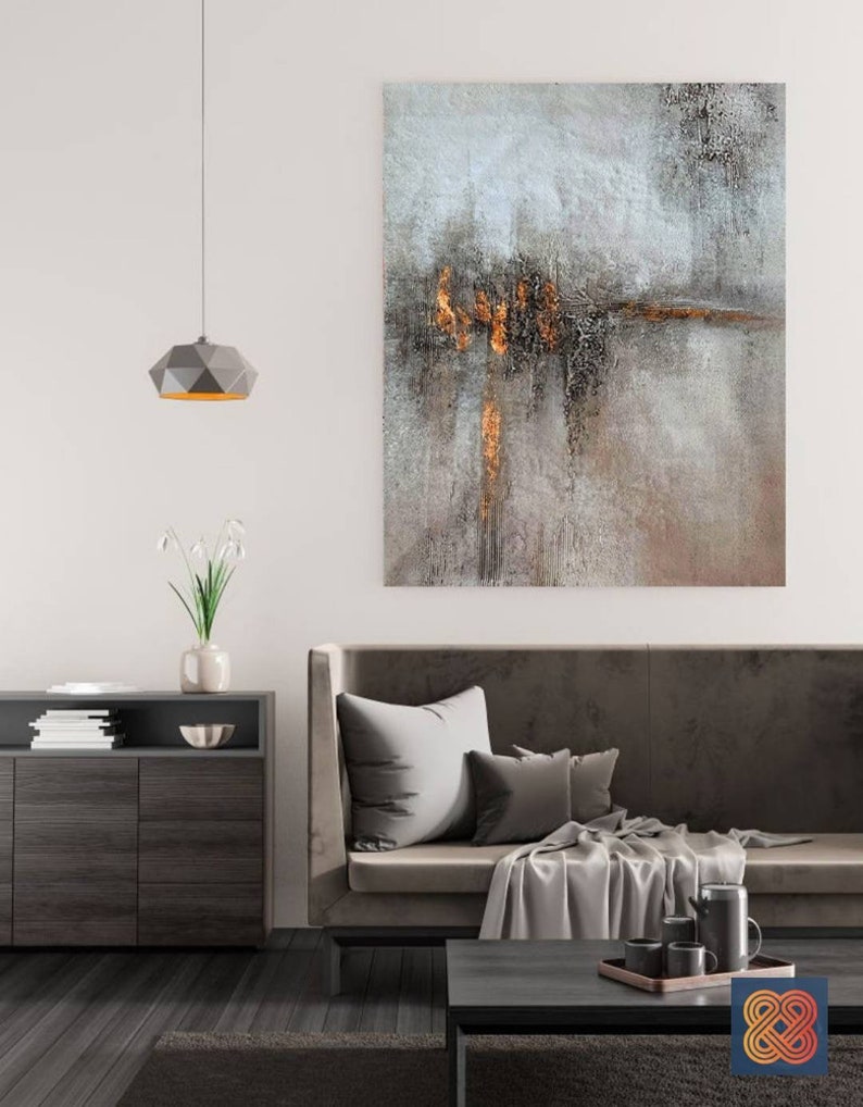 May include: A modern living room interior with a gray sofa, a coffee table, and a gray and gold abstract painting on the wall. The painting has a textured surface and features a horizontal line of gold paint.