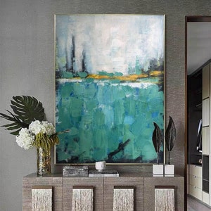 May include: Abstract painting with a green and blue color scheme. The painting is framed and hanging on a wall above a gray dresser.