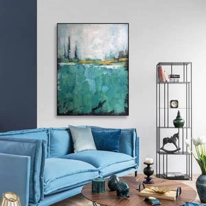 May include: Abstract painting with a green and blue color scheme. The painting is framed in black and hangs on a white wall above a blue sofa.