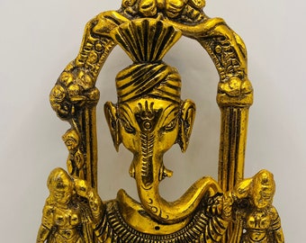 Puede incluir: Una estatua de metal dorado de Ganesha, el dios hindú de la sabiduría y la prosperidad, de pie en un arco decorativo con dos figuras femeninas a cada lado. La estatua está intrincadamente detallada y tiene un diseño tradicional.