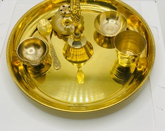 Op de afbeelding: Een gouden metalen dienblad met een bel, een lepel en vier kleine kommen. Het dienblad ligt op een wit oppervlak.