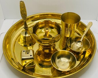 Op de afbeelding: Een set van zeven goudkleurige metalen voorwerpen voor een hindoeïstische puja-ceremonie, waaronder een bel, een kleine kom, een lepel, een beker, een klein schaaltje, een klein bakje en een dienblad.