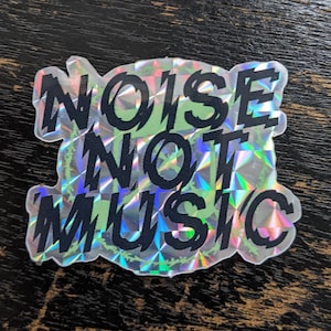 May include: A holographic sticker with the text "NOISE NOT MUSIC" in black lettering.