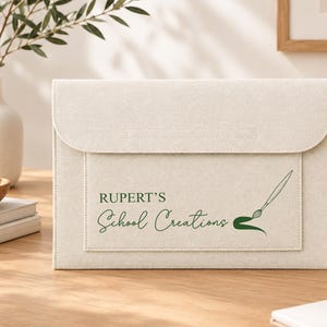 May include: A rectangular, off-white fabric document folder with a flap closure. The front features dark green text that reads "RUPERT'S School Creations" alongside a graphic illustration of a paintbrush with a green paint stroke.