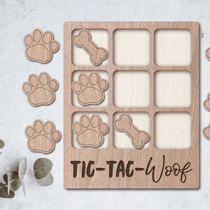 May include: A wooden tic-tac-toe game with paw prints and bone shapes. The game board has the text "TIC-TAC-Woof" written on it.