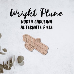 May include: A wooden cutout of a Wright Flyer airplane, with the text "Wright Plane, North Carolina, Alternate Piece" above it.