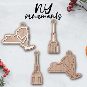 May include: Four wooden ornaments featuring New York City landmarks. Two ornaments are shaped like the state of New York with a heart inside, and two ornaments are shaped like the Empire State Building.