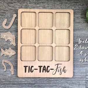 Puede incluir: Juego de tres en raya de madera con temática de peces. El tablero de juego tiene nueve casillas e incluye cuatro piezas: dos peces y dos anzuelos. El texto "TIC-TAC-Fish" está impreso en el tablero. El texto "Incluye 2 tableros y 4 opciones de piezas" está impreso en el lado derecho de la imagen.
