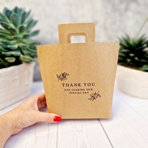 Könnte beinhalten: Eine braune Papiertüte mit Henkel. Die Tüte hat ein florales Design und den Text "Vielen Dank, dass Sie unseren besonderen Tag mit uns geteilt haben".
