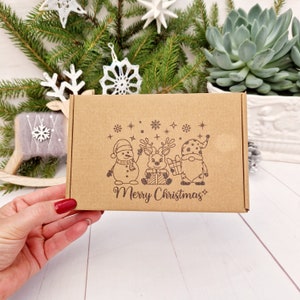 May include: A brown cardboard box with a Christmas-themed design. The box features a snowman, reindeer, and gnome holding gifts. The text "Merry Christmas" is printed on the box.