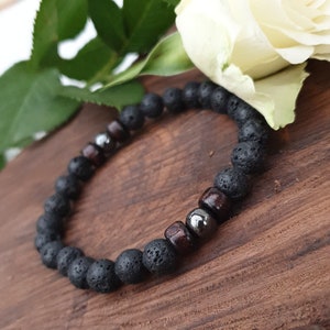 May include: Black lava rock and wood bead bracelet with silver accents. The bracelet is on a wooden surface.
