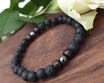 May include: Black lava rock and wood bead bracelet with silver accents. The bracelet is on a wooden surface.