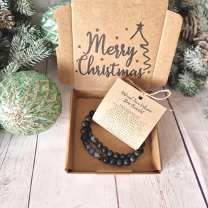 May include: A black lava stone bracelet presented in a brown box, the lid of which is printed with "Merry Christmas". A tag reads "Natural Lava Volcanic Stone Bracelet". The bracelet features black beads with blue and brown details.