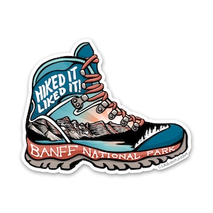 May include: A blue and white hiking boot with a mountain scene and the text "Hiked it Liked it!" on the side. The boot has a brown sole and the text "Banff National Park" on the bottom.