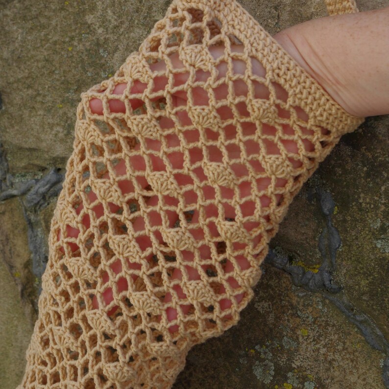 May include: A tan crochet sleeve with a diamond-shaped openwork pattern. The sleeve is made of a soft, textured yarn and has a ribbed cuff. The open design allows the skin to be visible through the crochet.