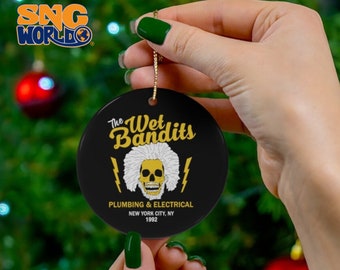 Può includere: Un ornamento natalizio in ceramica nera con la scritta "The Wet Bandits" in lettere dorate. L'ornamento presenta un teschio con capelli bianchi e fulmini. È incluso anche il testo "Plumbing & Electrical, New York City, NY 1992".