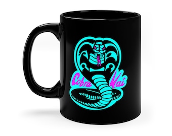 Puede incluir: Taza de café negra con un logotipo de cobra turquesa y el texto "Cobra Kai" en rosa.