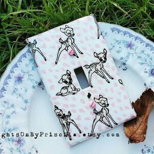 Könnte beinhalten: Eine weiße Lichtschalterabdeckung mit einem Muster aus schwarzen Rehen auf rosa Hintergrund und kleinen rosa Herzen. Die Abdeckung hat eine einzelne Schalteröffnung und rosa Schrauben. Der Etsy-Shop-Name ist sichtbar.