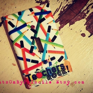 May include: A white light switch cover with a colorful pencil pattern and the text "Teachers Rock!" in black letters with a red apple graphic.