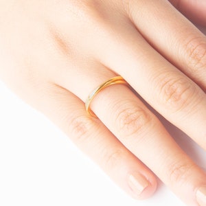 May include: A close-up of a hand wearing a thin gold band ring on the ring finger.