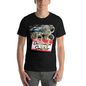 May include: A black t-shirt featuring a graphic of a green alien smoking a joint and wearing gold chains. The alien is holding a red name tag that reads "Hello, my name is... Designated Smoker".