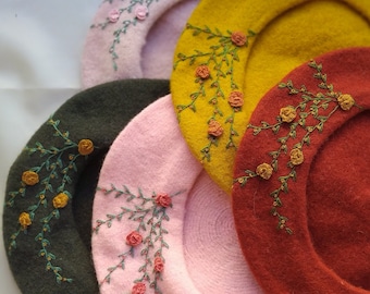 May include: Four berets in different colors, each with a floral embroidery design. The berets are stacked on top of each other, with the pink beret on top.
