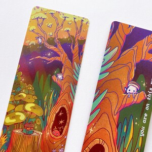 May include: Two colorful bookmarks with a whimsical forest scene. The bookmarks feature a large tree with a hollow trunk, a mushroom, and small white creatures. One bookmark has the text "you are on this page!" on the right side.