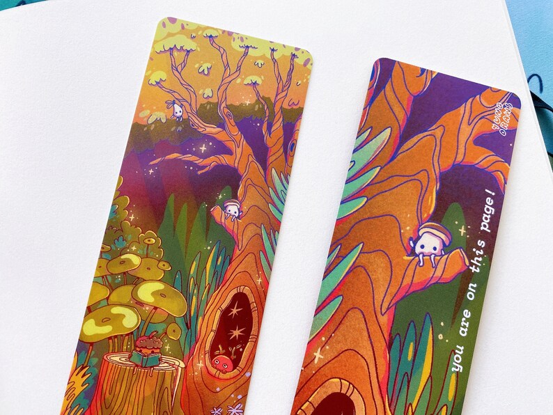 May include: Two colorful bookmarks with a whimsical forest scene. The bookmarks feature a large tree with a hollow trunk, a mushroom, and small white creatures. One bookmark has the text "you are on this page!" on the right side.