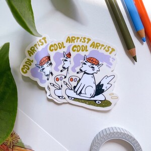 Puede incluir: Tres pegatinas con un perro de dibujos animados que lleva un sombrero y sostiene un pincel, montando un monopat&iacute;n. Las pegatinas tienen el texto "Cool Artist" en letras amarillas sobre un fondo morado.
