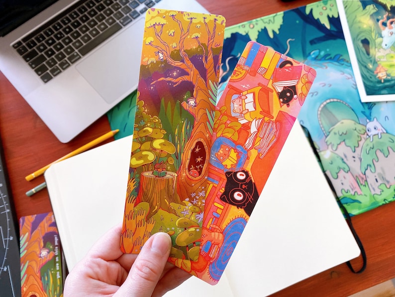 May include: Two colorful bookmarks with illustrations of a forest scene and a cat reading a book. The bookmarks are made of sturdy cardstock and are perfect for marking your place in a book.