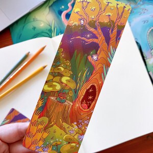 May include: A colorful bookmark featuring a whimsical illustration of a tree with a hollow trunk, a small creature peeking out, and a mushroom forest. The bookmark is printed on thick cardstock and has a glossy finish.