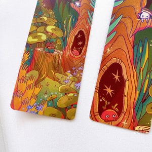 May include: Two colorful bookmarks with whimsical illustrations of a forest scene. The bookmarks feature a tree trunk with hollow spaces, mushrooms, and small creatures. One bookmark has the text "you are on this page" on the right side.