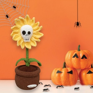 May include: A crocheted sunflower with a skull face in a brown pot, surrounded by black spiders and orange pumpkins with jack-o'-lantern faces.