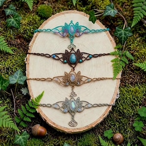 May include: Four macrame bracelets arranged vertically, each featuring a central oval gemstone, intricate knotted cord patterns, and small accent beads. The bracelets are crafted in teal, dark brown, tan, and grey, with metal lotus or knot charms.