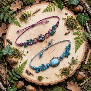 Pode incluir: Duas pulseiras de macramé com pedras ovais centrais em engastes de latão. A pulseira superior é roxa com contas de ametista e detalhes de folhas verdes. A pulseira inferior é azul-clara com contas azuis e folhas verdes, ambas com cordões ajustáveis.