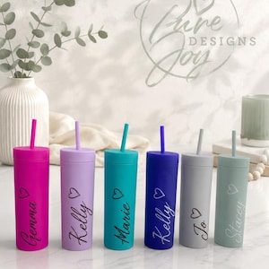 May include: Six brightly coloured tumblers with straws, in shades of pink, lilac, teal, blue, grey, and sage green. Each tumbler has a name and a heart symbol printed on it. The tumblers are cylindrical and have matching coloured straws.