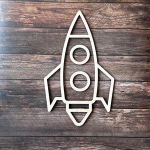 May include: A white wooden rocket ship cutout with two round windows and a pointed nose. The rocket is on a brown wooden background.