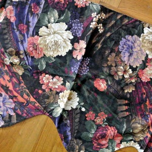 May include: A floral fabric with a dark background, featuring large white, pink, and purple flowers. The fabric has a detailed pattern with various floral arrangements and a mix of colors, including orange and green.