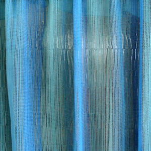 Puede incluir: Un primer plano de una cortina transparente azul y turquesa con textura tejida. La cortina está hecha de hilos finos que se tejen juntos para crear una tela delicada y aireada.