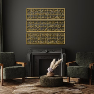May include: Three gold framed pieces of Islamic calligraphy hang on a black wall above a fireplace. The fireplace has a black mantel and a black interior. There is a green armchair on the right and a green armchair on the left. A small round ottoman sits in front of the fireplace.