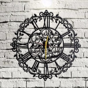 Op de afbeelding: Zwarte metalen wandklok met Romeinse cijfers en Arabische kalligrafie in een cirkelvormig ontwerp. De klok heeft een decoratief, versierd frame.