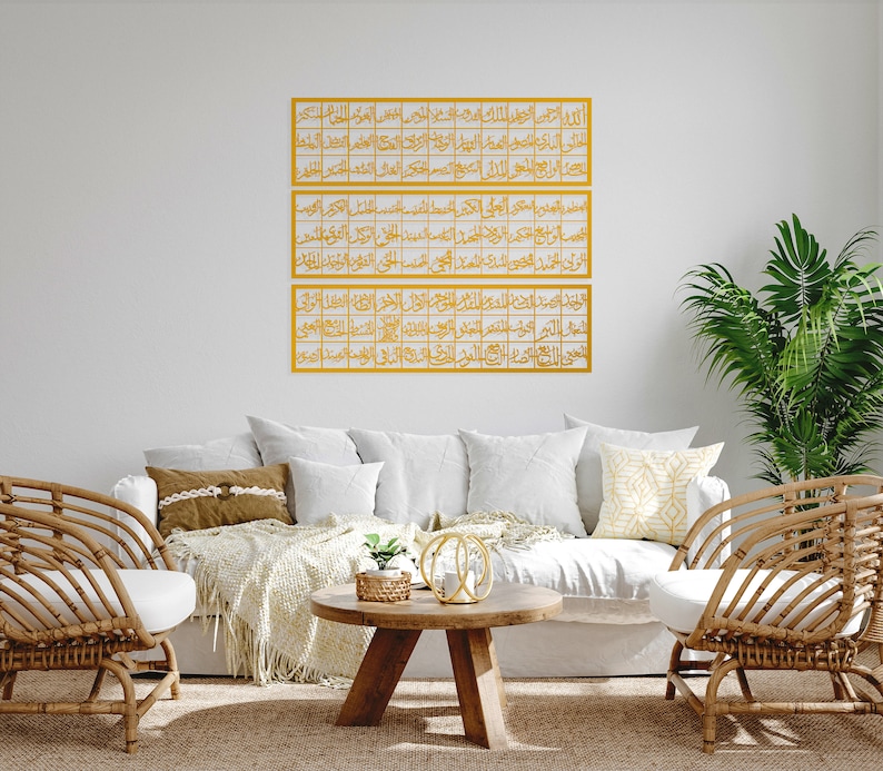 May include: Three gold framed pieces of Islamic calligraphy hang on a white wall above a white couch with pillows and a throw blanket. Two wicker chairs are on either side of the couch. A small wooden table with a plant and a decorative object sits in front of the couch.