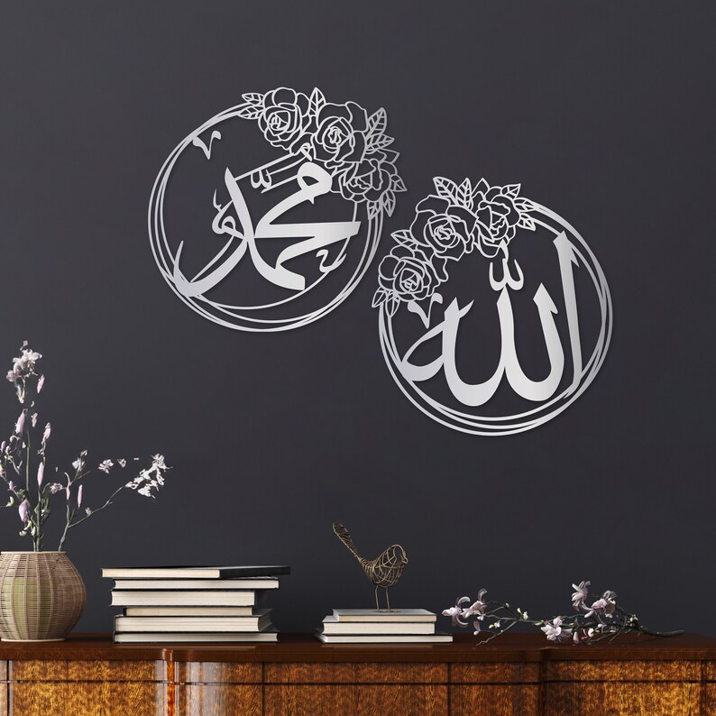 K&ouml;nnte beinhalten: Zwei silberne Wanddekorationen aus Metall mit floralen Designs. Das linke St&uuml;ck zeigt das arabische Wort "Muhammad" in einem runden Rahmen. Das rechte St&uuml;ck zeigt das arabische Wort "Allah" in einem runden Rahmen.