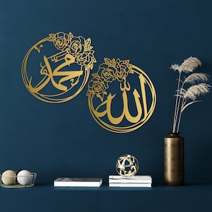 K&ouml;nnte beinhalten: Zwei goldene Wanddekorationen aus Metall mit floralen Designs. Das linke St&uuml;ck zeigt das arabische Wort f&uuml;r "Muhammad" und das rechte St&uuml;ck zeigt das arabische Wort f&uuml;r "Allah".
