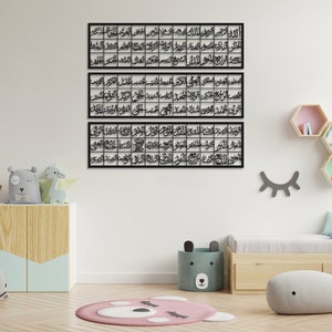 May include: Three black metal wall art pieces with Arabic calligraphy in a white room with a wooden shelf and a bed with pillows and a gray whale stuffed animal.